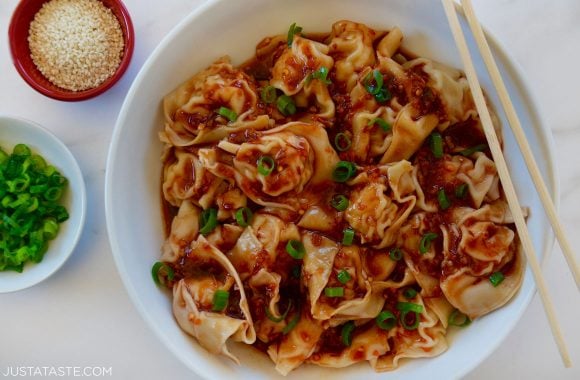 Bowl containing Spicy Chicken Wontons with chopsticks garnished with scallions and sesame seeds