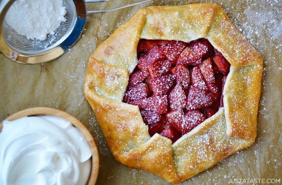 Strawberries and cream galette garnished with powered sugar next to bowl containing whipped cream