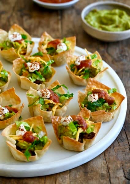 Taco cups featuring crispy baked wonton wrappers filled with seasoned taco meat and topped with shredded lettuce, shredded cheese and a dollop of sour cream.