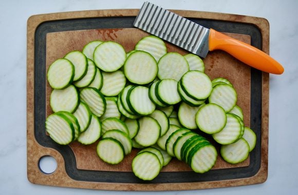 A serrated knife on a wood cutting board with sliced zucchini