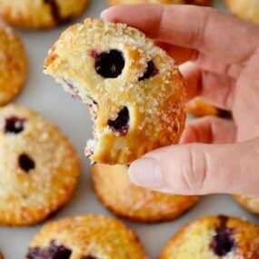 A hand holding a blueberry hand pie with more hand pies in the background