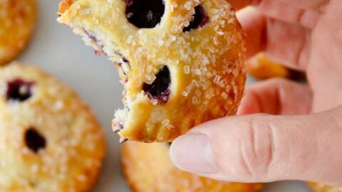 A hand holding a blueberry hand pie with more hand pies in the background