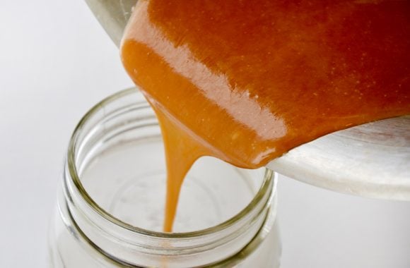 The best boozy caramel sauce being poured into glass jar