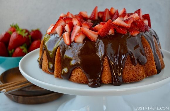 A white cake plate containing a cake topped with chocolate glaze and strawberries