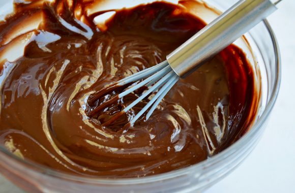 A glass bowl containing melted chocolate with a whisk