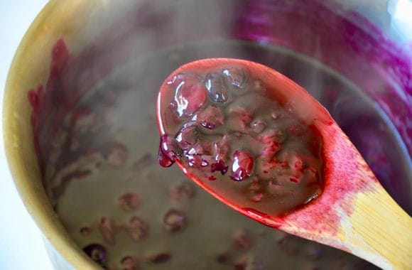 Wooden spoon over sauce pan containing easy homemade blueberry sauce