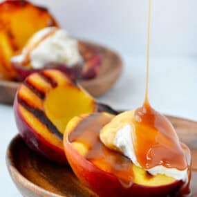 Grilled peaches with vanilla ice cream being drizzled with caramel sauce.