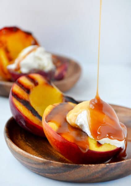 Grilled peaches with vanilla ice cream being drizzled with caramel sauce.