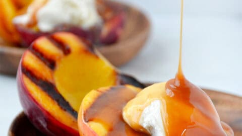 Grilled peaches with vanilla ice cream being drizzled with caramel sauce.