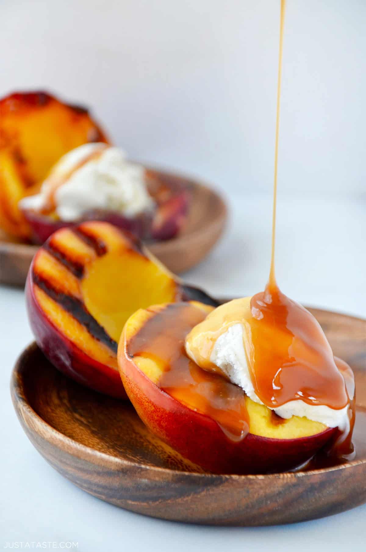 Grilled peaches with vanilla ice cream being drizzled with caramel sauce.