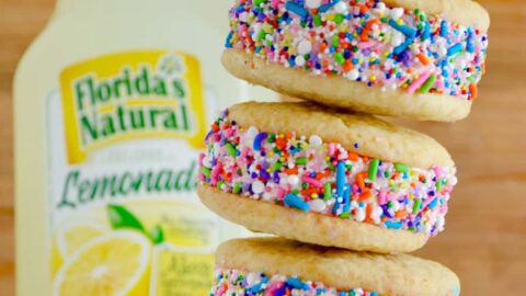 A stack of lemon ice cream sandwiches coated in sprinkles with a bottle of lemonade behind them