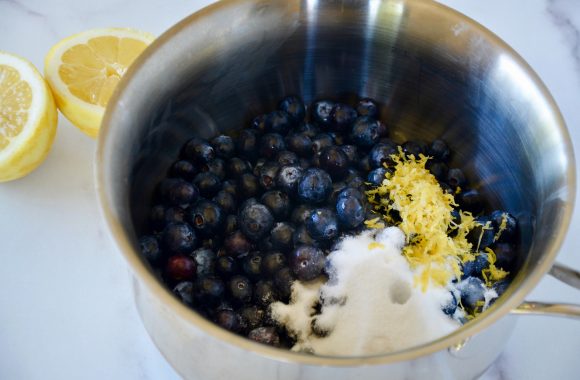 Sauce pan containing fresh blueberries, lemon zest and sugar