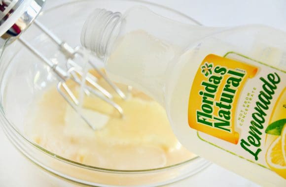 A bottle of lemonade being poured into a clear bowl containing cream cheese