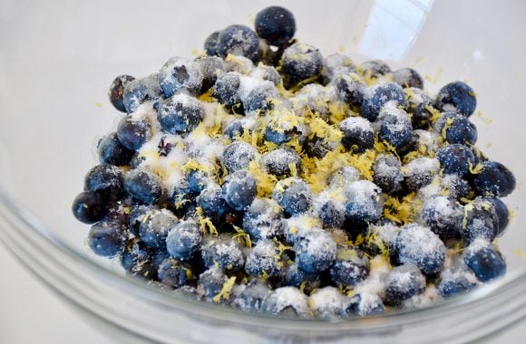 A glass bowl containing blueberries, lemon zest and sugar