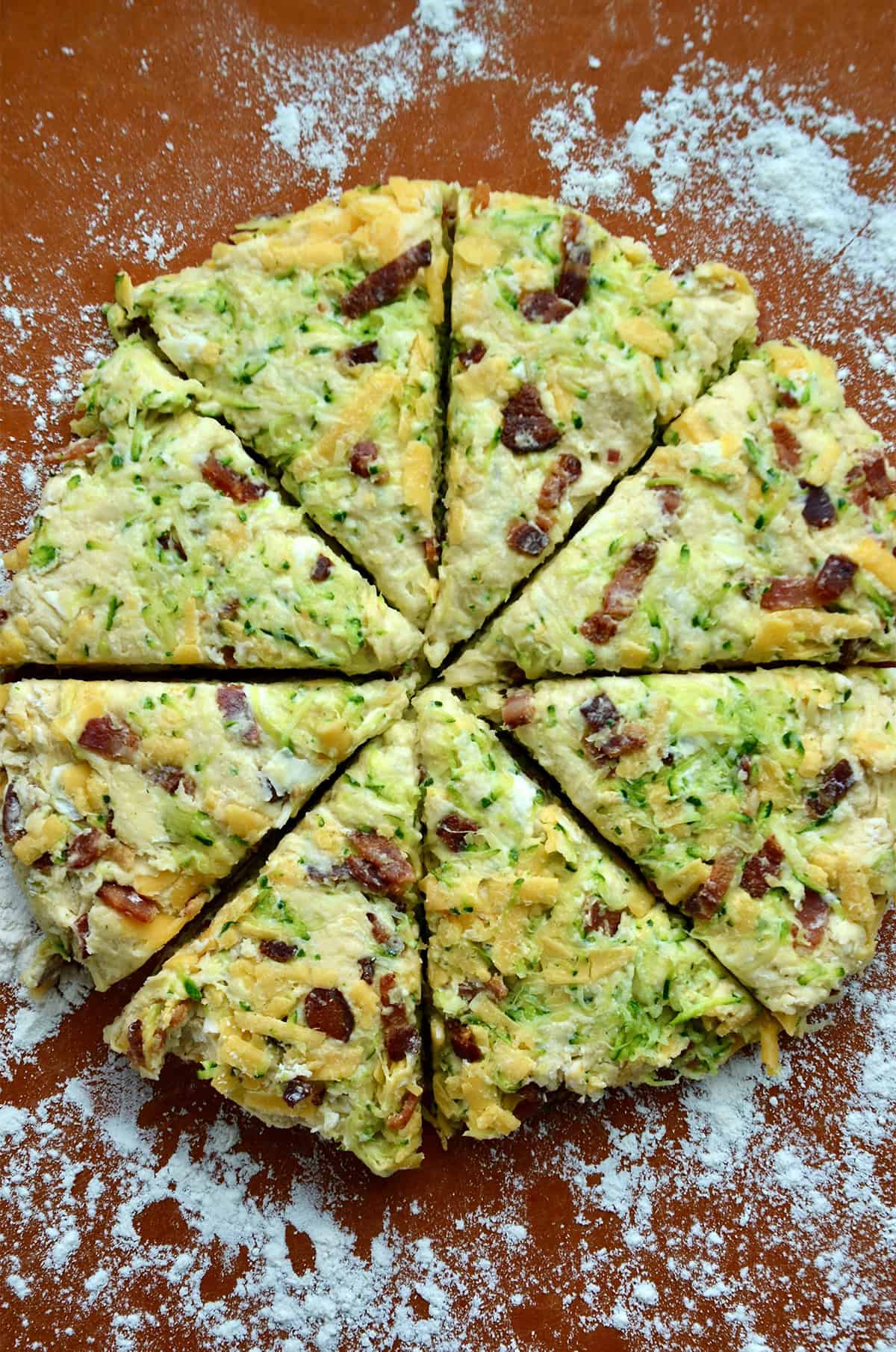 A disc of zucchini cheddar scone dough cut into eight wedges.