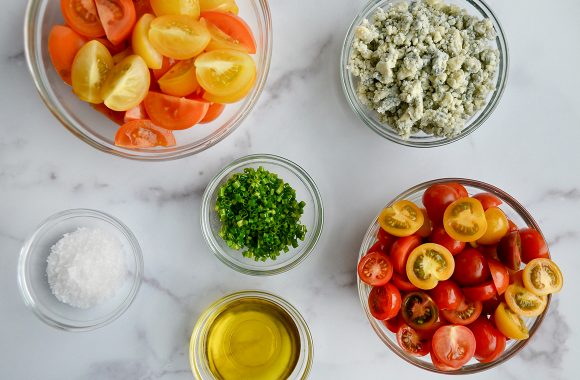 Small glass bowls filled with cherry tomatoes, chives, blue cheese, olive oil and salt