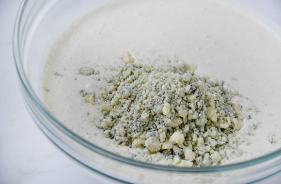 Clear bowl containing buttermilk dressing with blue cheese crumbles
