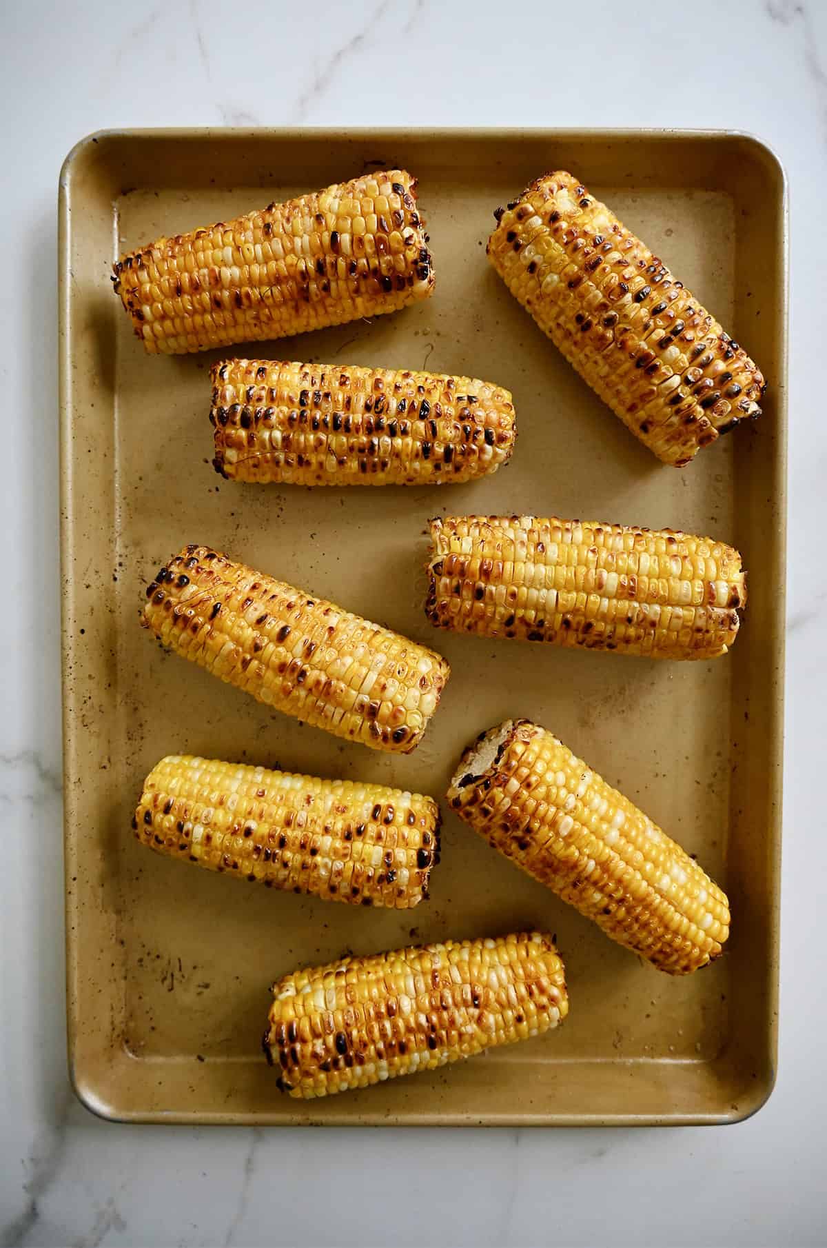 Blistered corn on the cob on a baking sheet.