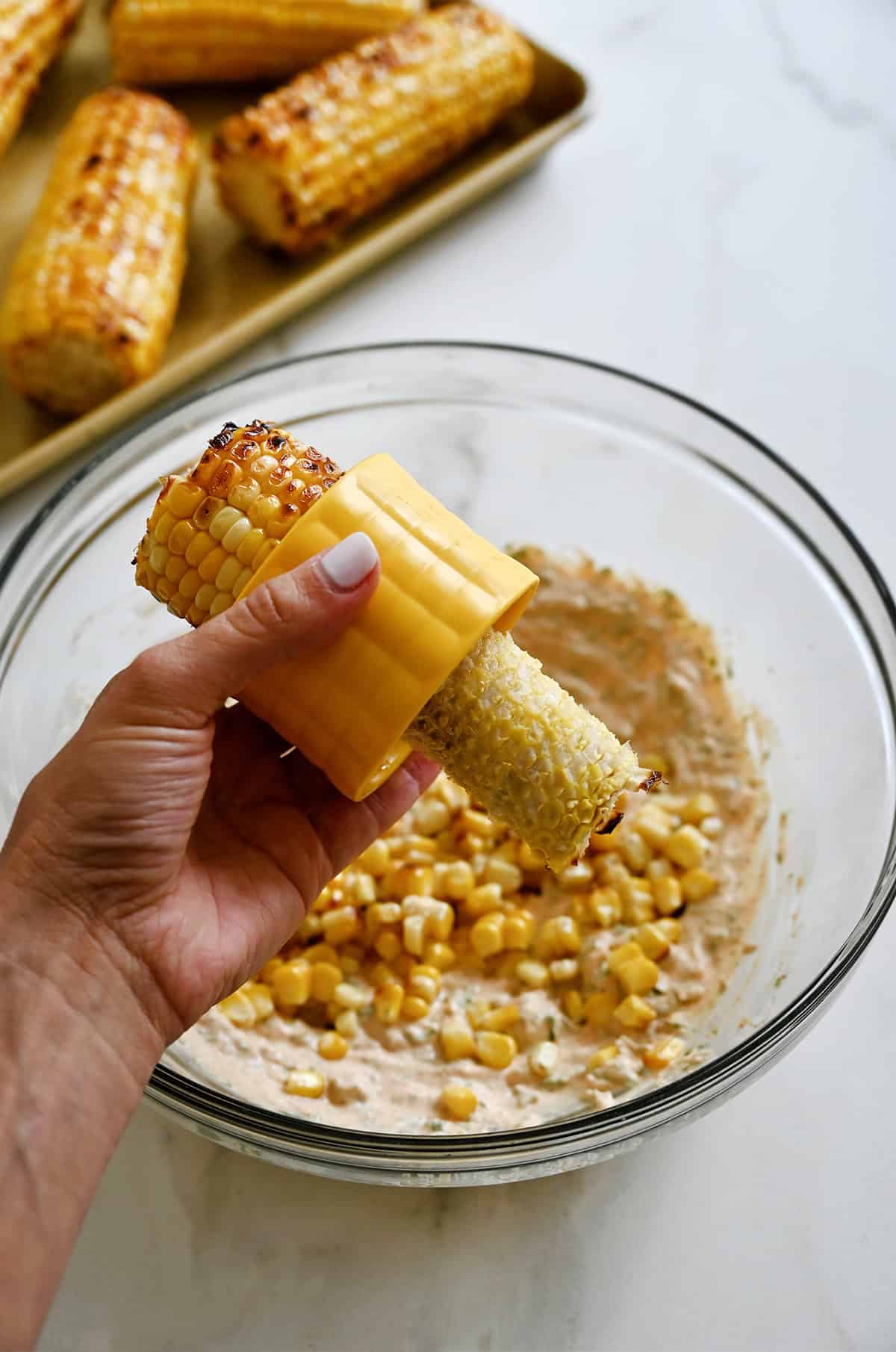 A corn stripping tool removes corn kernels from an ear of corn over a bowl.