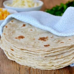 A stack of homemade flour tortillas in a blue towel.