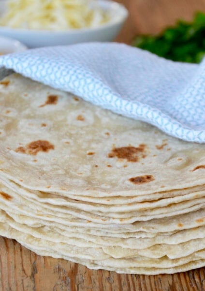 A stack of homemade flour tortillas in a blue towel.