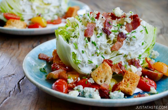 Plate containing iceberg wedge salad with buttermilk dressing topped with chopped bacon, blue cheese crumbles, cherry tomatoes, chives and croutons