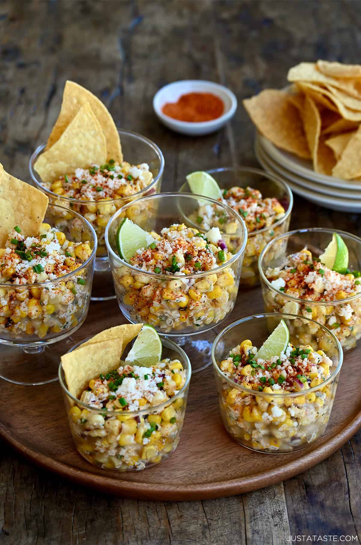 Individual cups of elote salad topped with Cotija cheese, served alongside tortilla chips for dipping.