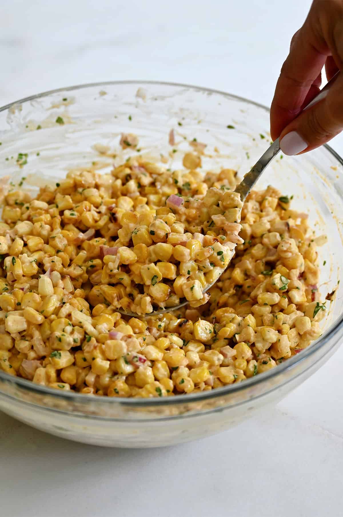 Blistered corn kernels coated in a smoky, tangy dressing in a large mixing bowl. 
