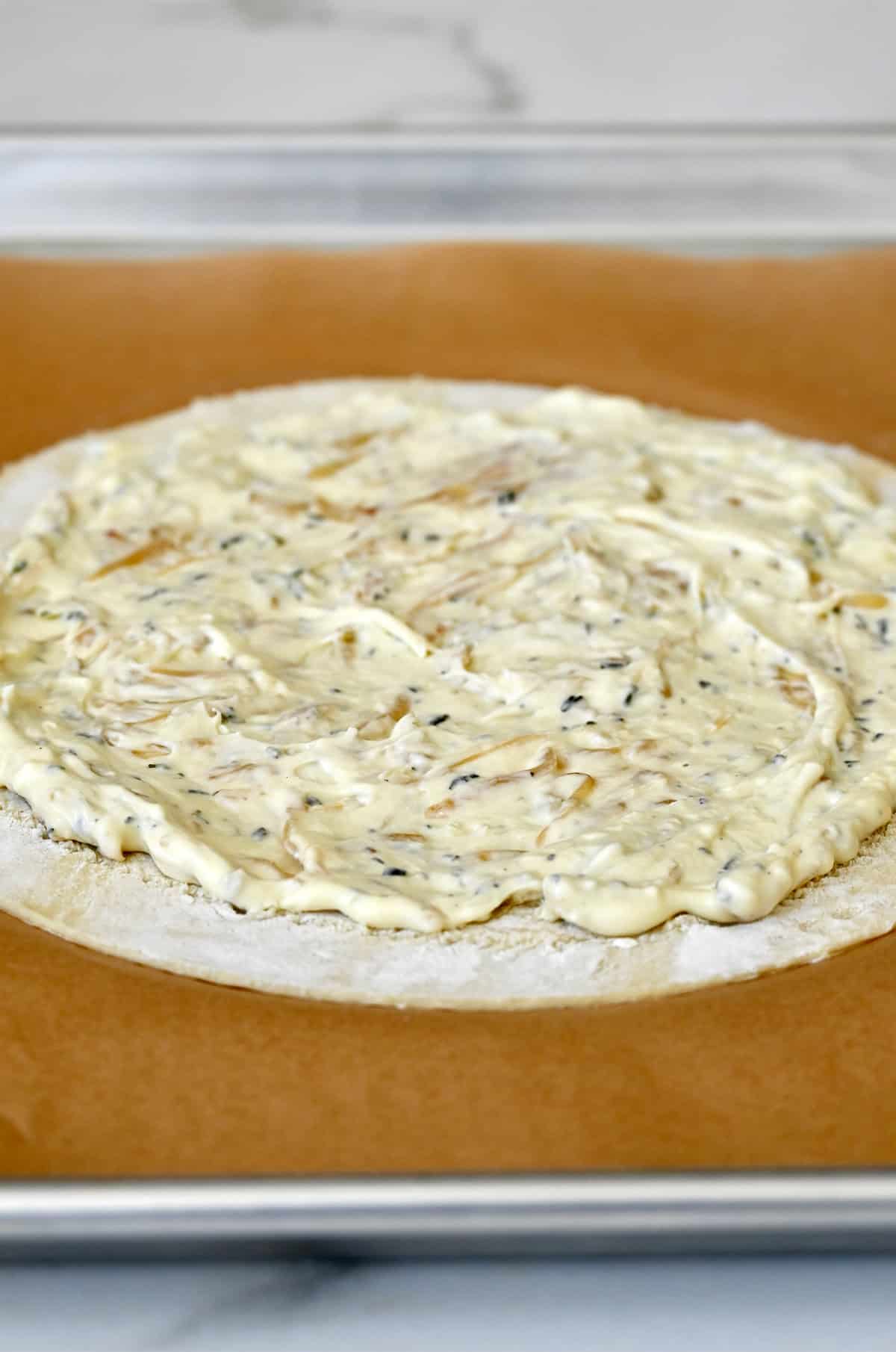 Caramelized onion cheese spread slathered atop puff pastry on a parchment paper-lined baking sheet.