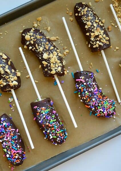 Frozen chocolate covered bananas with popsicle sticks on a baking sheet.