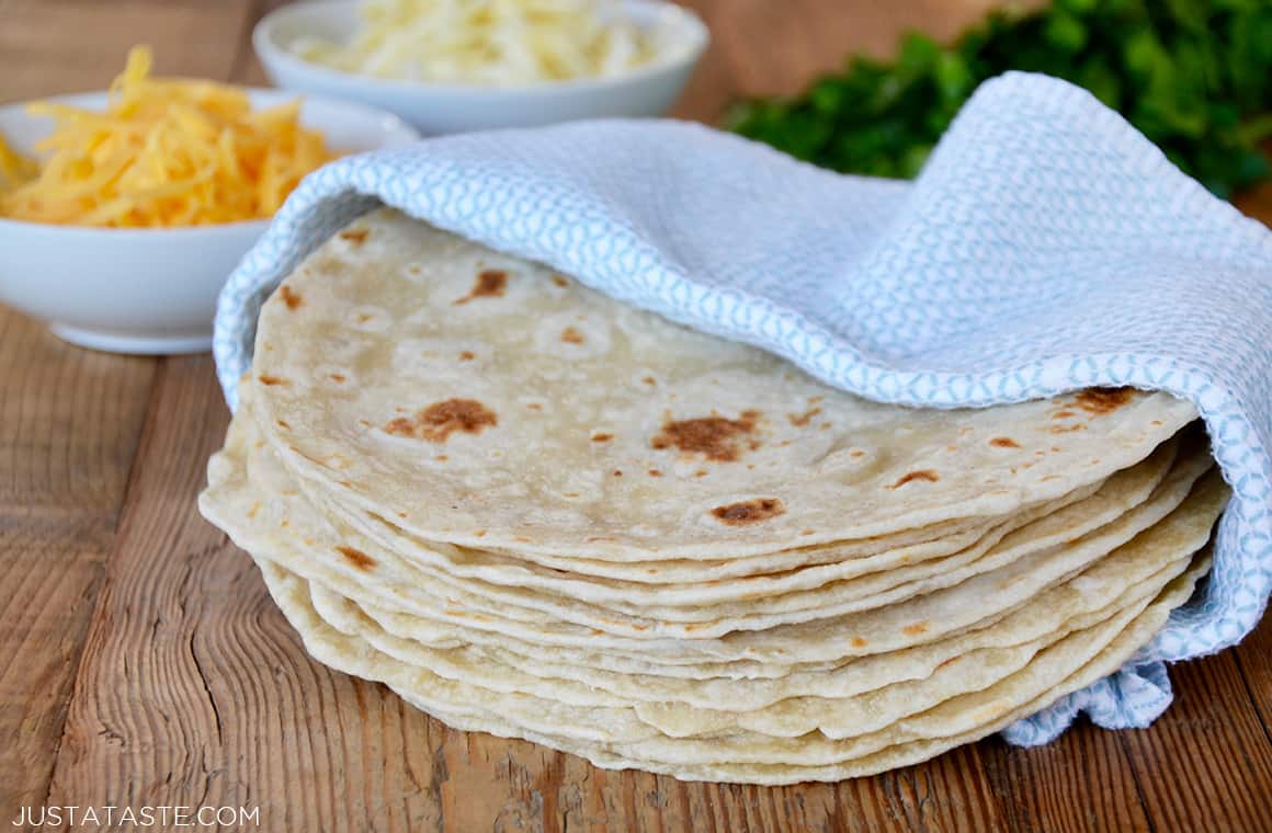 A stack of homemade flour tortillas in a blue towel