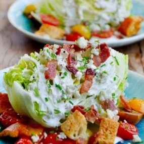 Easy iceberg wedge salad with buttermilk dressing topped with chopped bacon on plate with croutons and cherry tomatoes