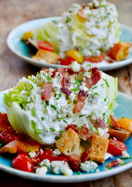 Easy iceberg wedge salad with buttermilk dressing topped with chopped bacon on plate with croutons and cherry tomatoes