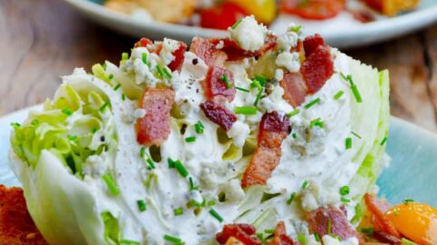 Easy iceberg wedge salad with buttermilk dressing topped with chopped bacon on plate with croutons and cherry tomatoes