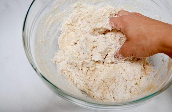 A glass bowl with tortilla dough being mixed by hand