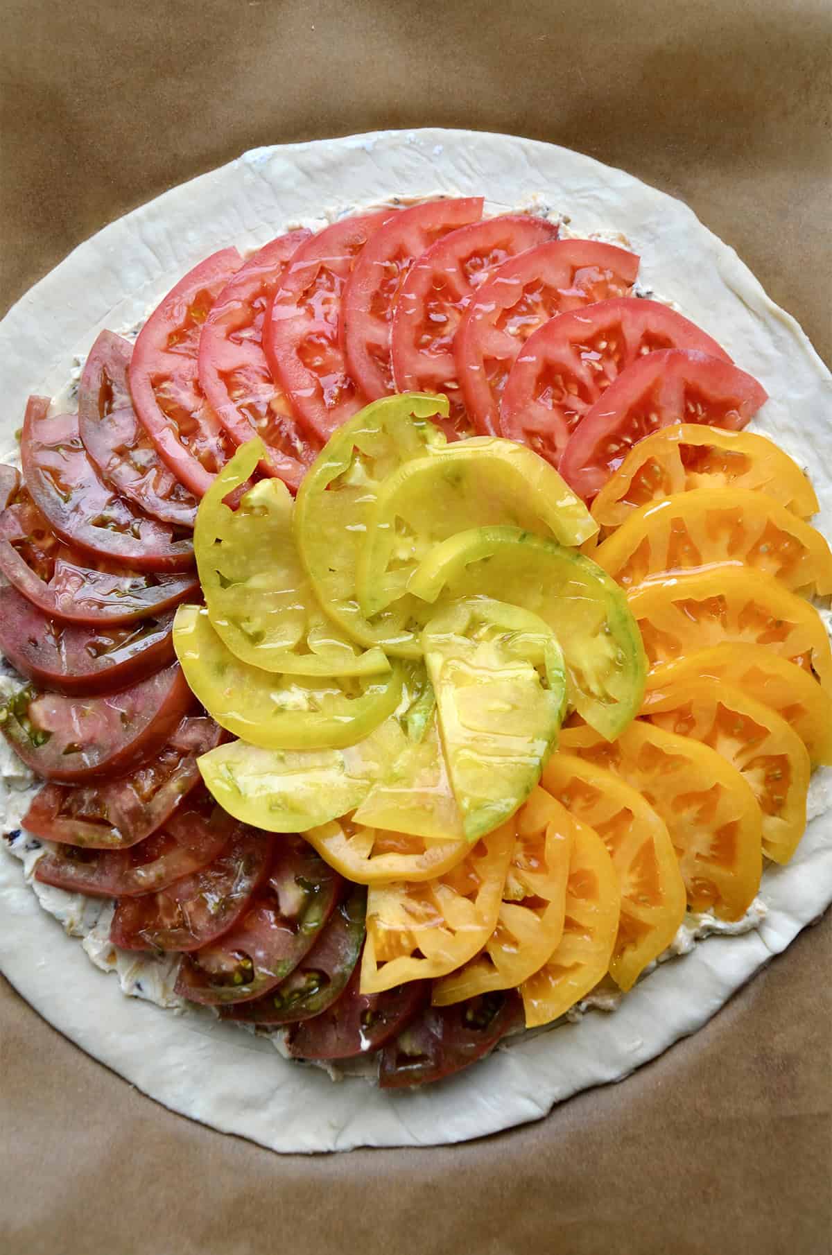 Unbaked tomato puff pastry tart on a parchment paper-lined baking sheet.