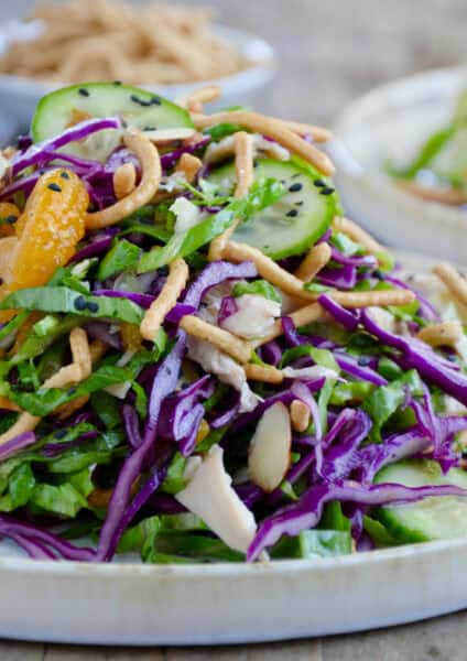 Chinese chicken salad with sesame dressing, mandarin oranges, sliced cucumbers, crispy chow mein noodles and sliced almonds on a salad plate.