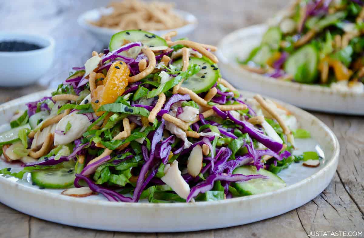 Chinese chicken salad with sesame dressing, mandarin oranges, sliced cucumbers, crispy chow mein noodles and sliced almonds on a salad plate.