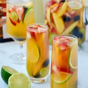 Various glasses filled with the best homemade white sangria with strawberries, limes, apples, grapes, blackberries and peaches