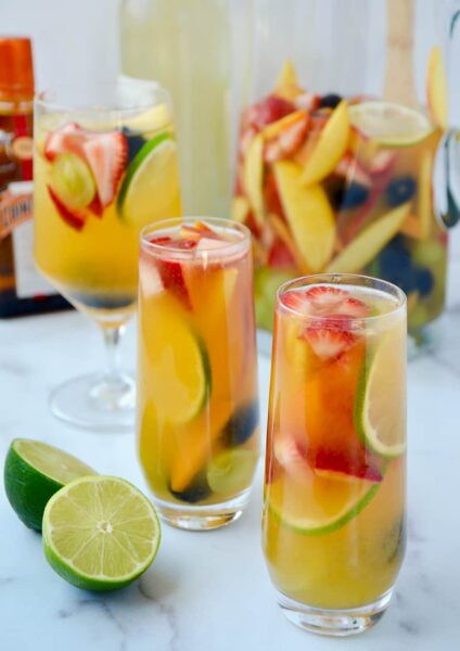 Various glasses filled with the best homemade white sangria with strawberries, limes, apples, grapes, blackberries and peaches