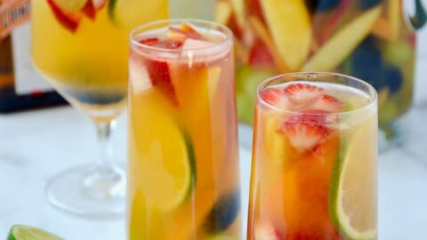 Various glasses filled with the best homemade white sangria with strawberries, limes, apples, grapes, blackberries and peaches