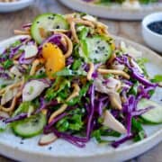 A white plate containing Chinese Chicken Salad with crunchy noodles, mandarin orange slices and sliced cucumber.