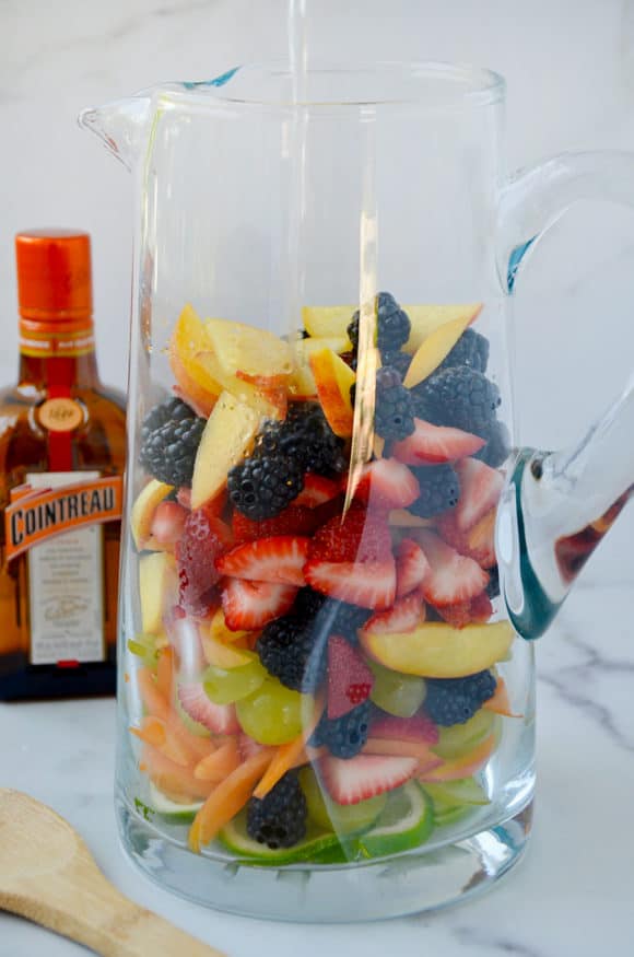Pitcher containing chopped fresh fruit with orange liqueur in the background