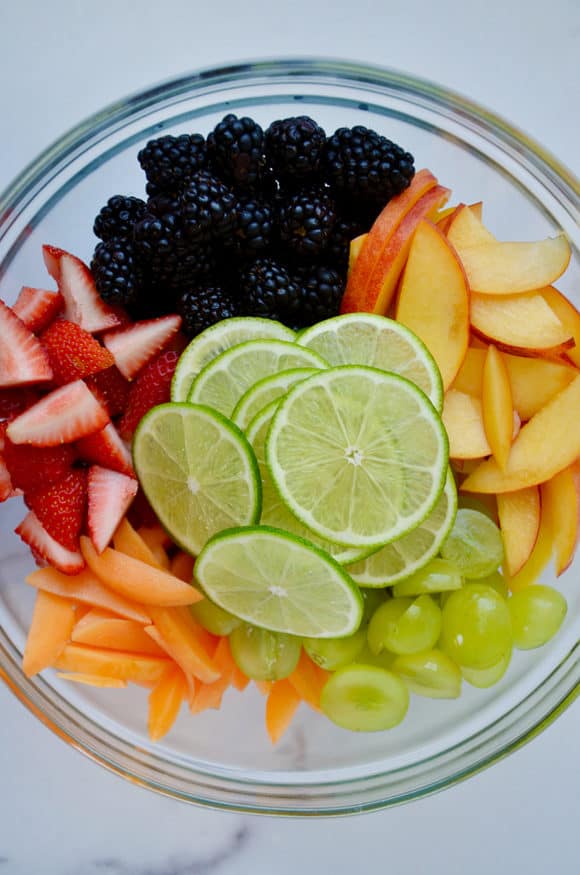 Glass bowl with sliced limes, blackberries, apples, grapes, peaches and strawberries