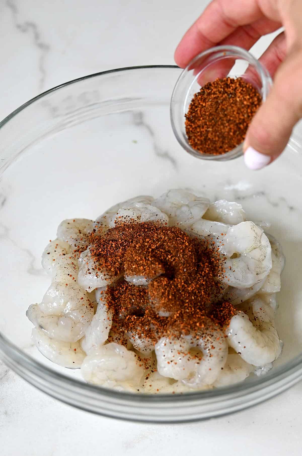 Adding Chinese five-spice atop uncooked shrimp in a bowl.