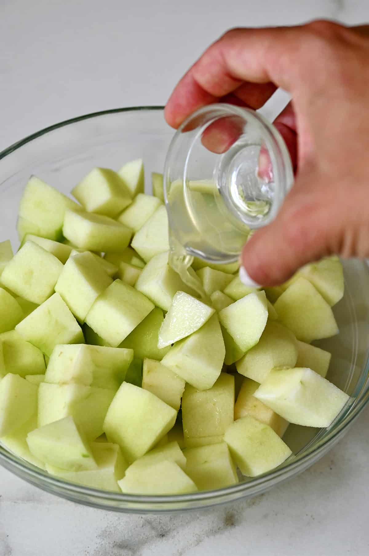 Tossing diced apples with lemon juice in a glass bowl.