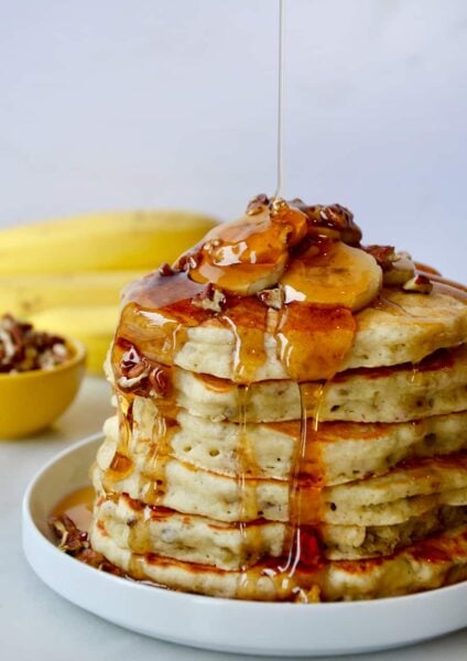 A tall stack of banana pancakes topped with bananas and maple syrup