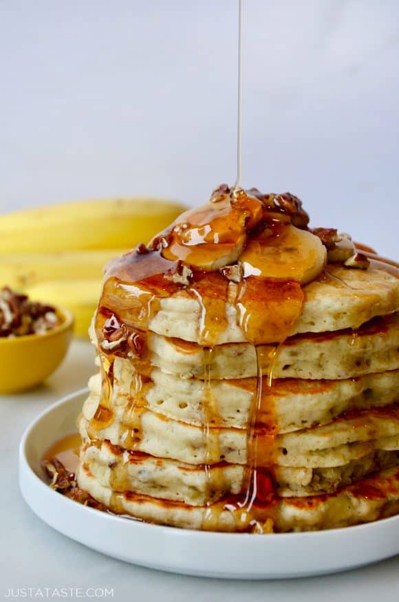 A tall stack of banana pancakes topped with bananas and maple syrup