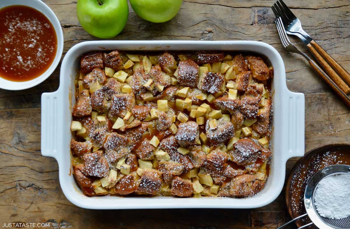 Apple bread pudding baked with brioche and Granny Smith apples in a white 9x13 baking dish, finished with a drizzle of bourbon caramel sauce.
