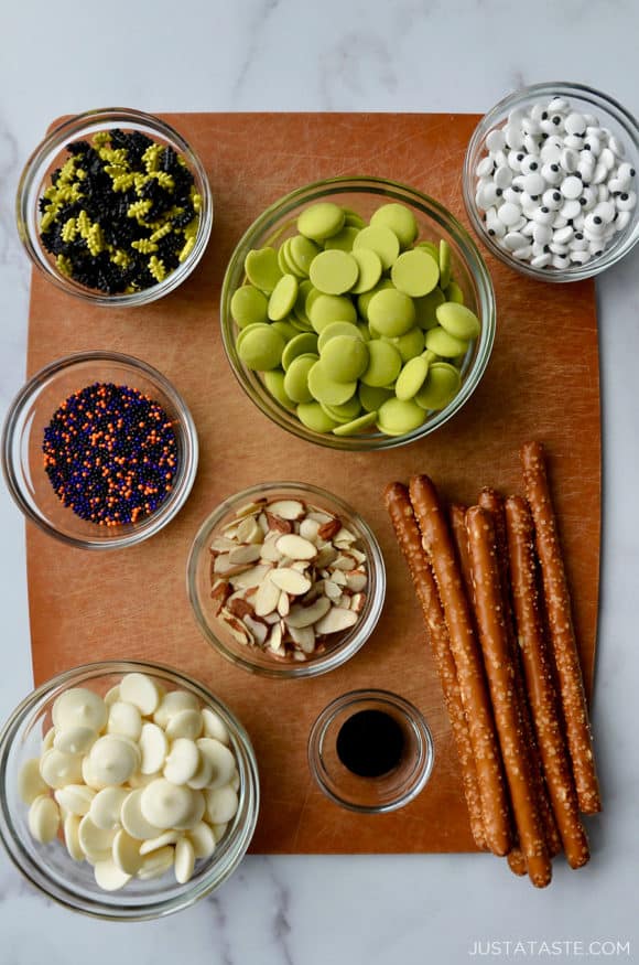 A cutting board containing glass bowls with ingredients for making chocolate pretzels